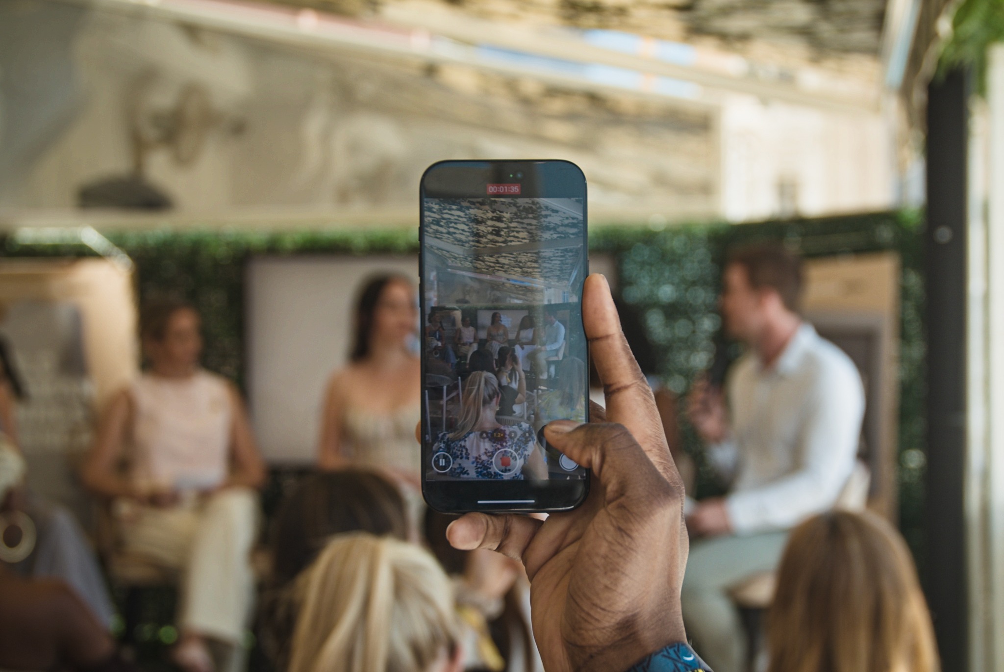 hand holding a phone and filming people on stage who are visible through the phone screen