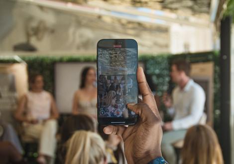 hand holding a phone and filming people on stage who are visible through the phone screen